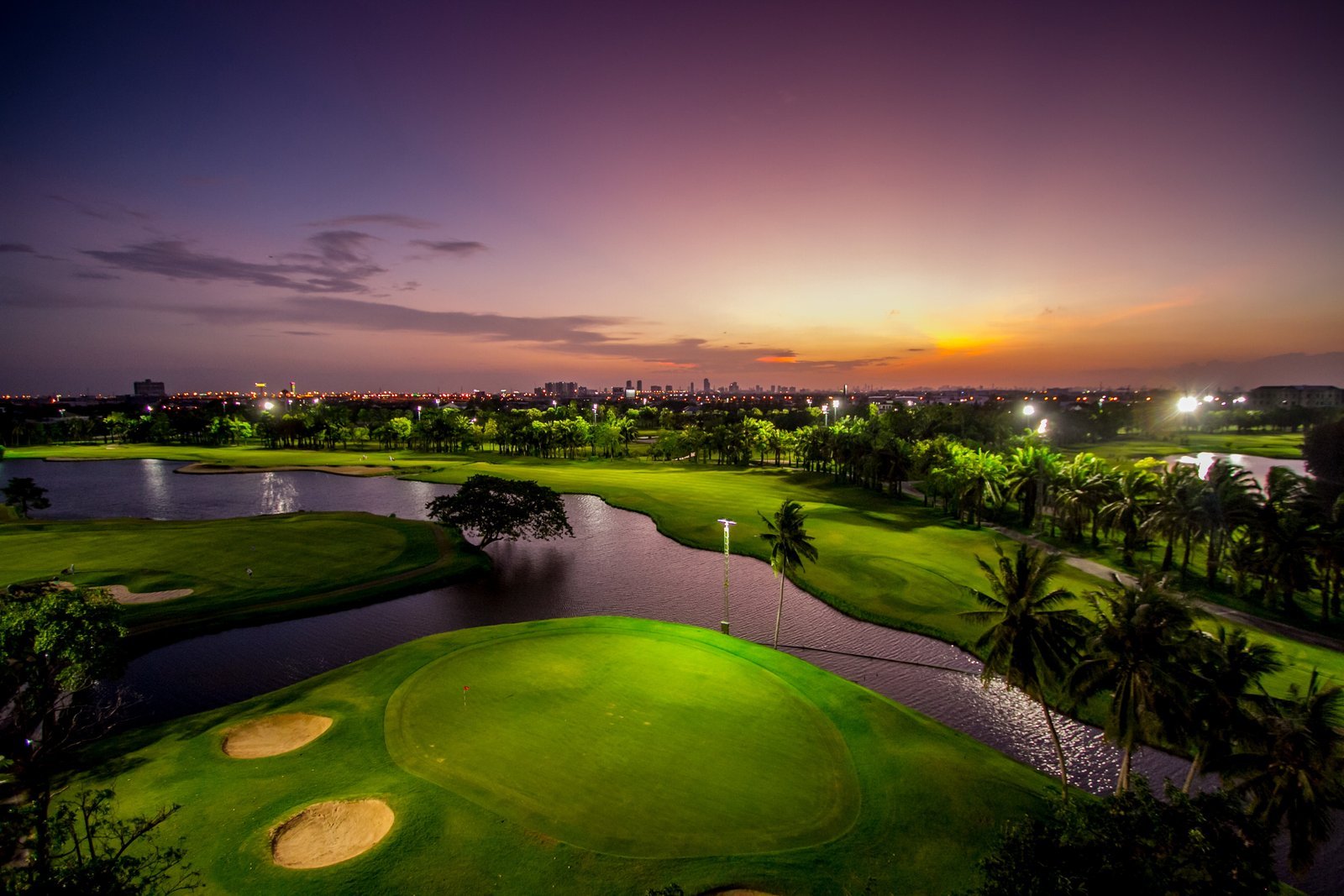 Night golf under floodlights at Summit Windmill Golf Club, with the Bangkok skyline beyond